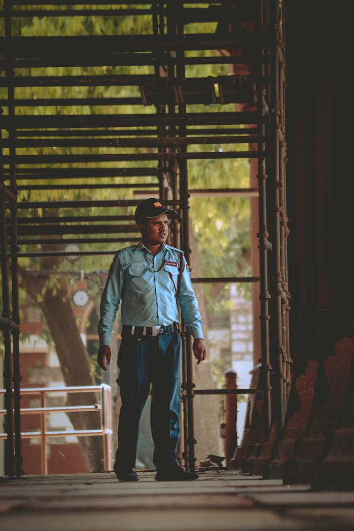 A security guard stands watchfully in a construction area, framed by scaffolding.